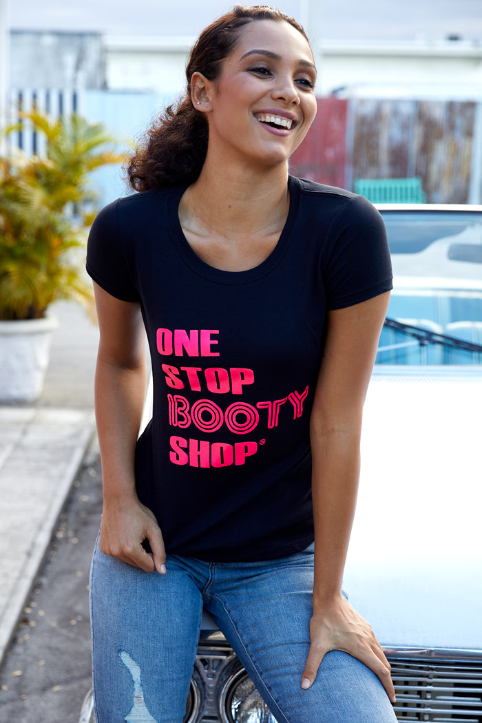 Model wearing the One Stop Booty Shop Graphical Tee in black with bright pink text, showcasing a fun 70's vibe.